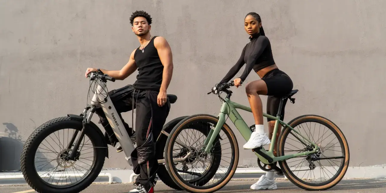 A man and woman pose with their electric bikes. This shows what a hybrid bike is good for: versatile riding on various terrains, blending comfort and performance for urban commutes or light trails.