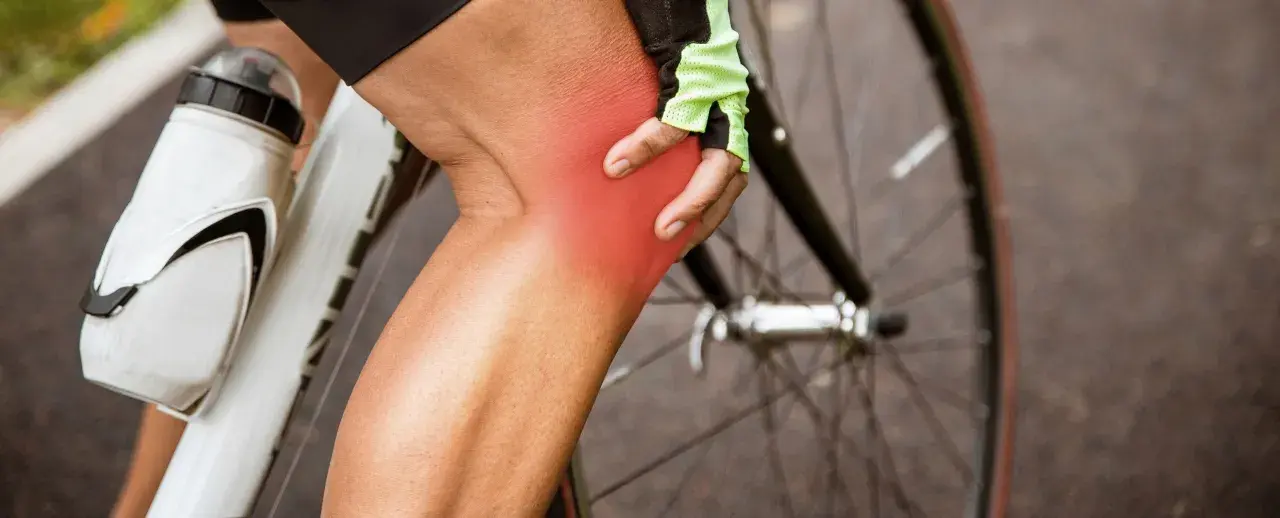 Cyclist holding knee with red pain indicator. Learn about cycling knee pain exercises to get back on the road.