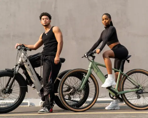 A man and woman pose with their electric bikes. This shows what a hybrid bike is good for: versatile riding on various terrains, blending comfort and performance for urban commutes or light trails.