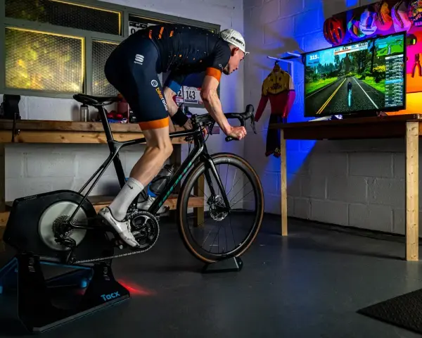 Cyclist on a Tacx trainer, connected to a TV displaying a Zwift course. This setup showcases Zwift compatible devices for an immersive indoor cycling experience.