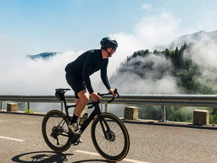 A cyclist in black gear conquers a mountain road, enjoying the breathtaking views and the freedom of long rides amidst swirling clouds.