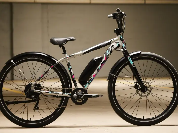 A white GT power performer electric bike with a colorful geometric pattern, parked indoors.