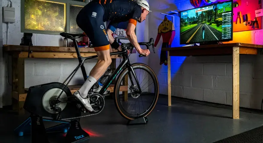 Cyclist on a Tacx trainer, connected to a TV displaying a Zwift course. This setup showcases Zwift compatible devices for an immersive indoor cycling experience.