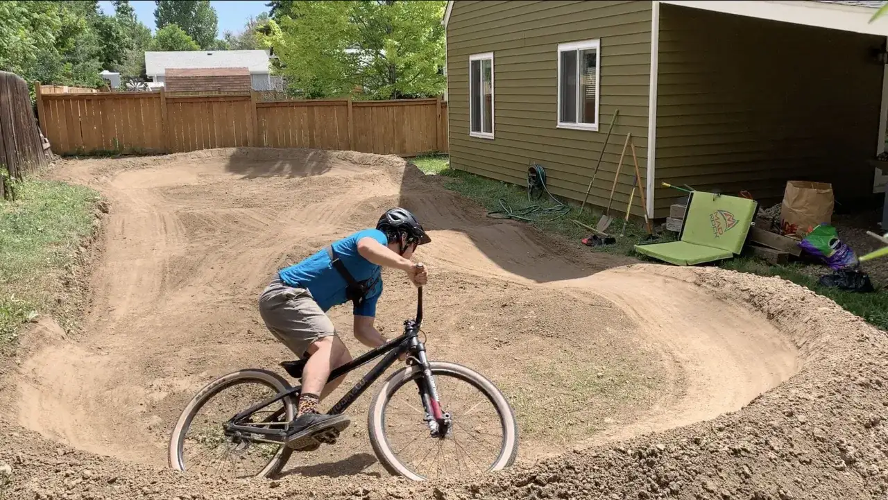 A rider on a dirt bike navigates a newly built backyard pump track, ready for some serious air.