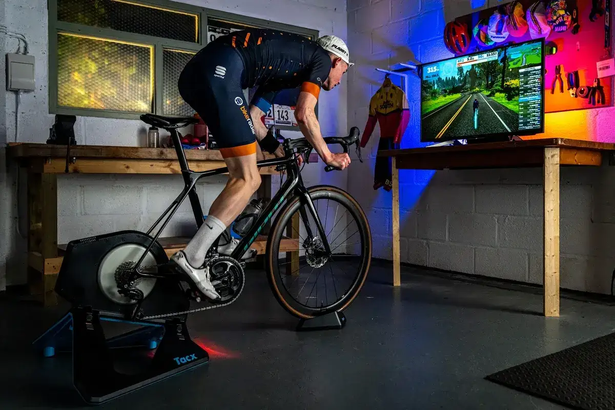 Cyclist on a bike trainer, a device that allows indoor cycling, rides in front of a screen displaying a virtual road.