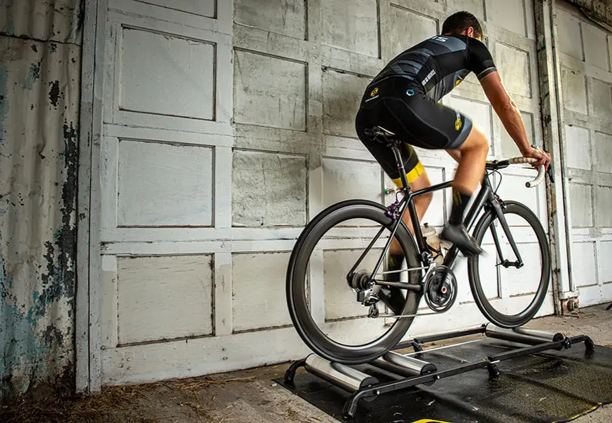 Cyclist training indoors on a bike roller vs trainer setup. The bike is on rollers, requiring balance.