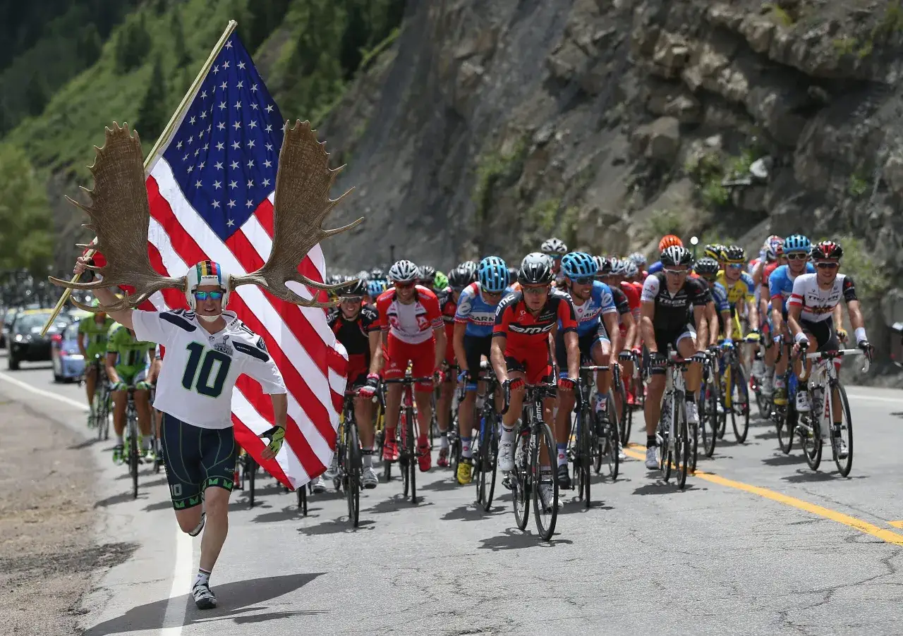 A fan with moose antlers and an American flag cheers on cyclists during the Dauphin&eacute; cycling race.