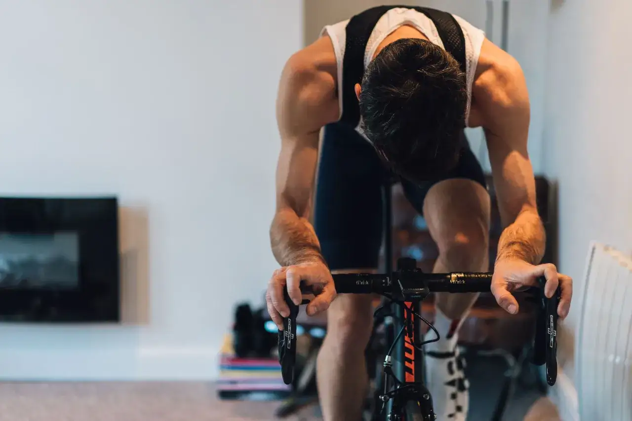 A cyclist trains indoors, head down, focused on their 12 week cycling training plan.