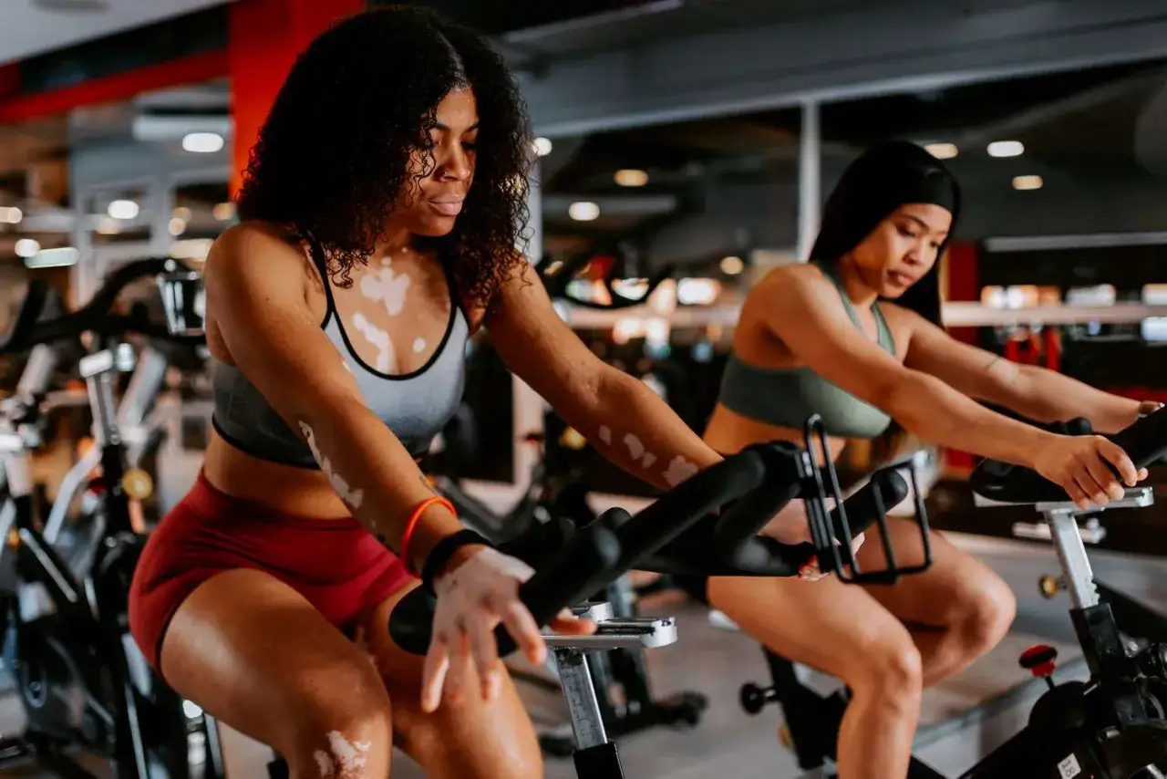 Two women cycle intensely, showcasing the pros and cons of stationary bikes: a great cardio workout, but can be monotonous.